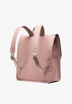 Vaaleanpunainen, suorakaiteen muotoinen reppu, joka on valmistettu sileästä kankaasta. Varustettu pehmustetuilla olkahihnoilla, sivutaskulla ja yläpiedellä. Yksinkertaiset saumat ja strukturoitu hihnapinnoite.