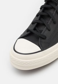 Czarne siateczkowe trampki z białym gumowym noskiem i podeszwą. Posiada płaskie czarne sznurówki oraz teksturowaną cholewkę. Diamentowy wzór na podeszwie.