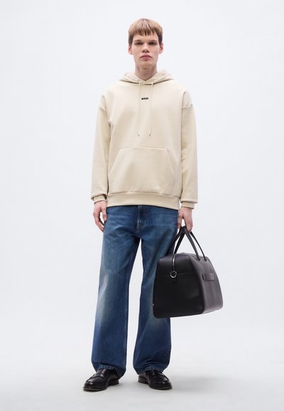 Sweat à capuche beige avec une poche kangourou et un logo, jean bleu à jambes larges, et sac en cuir noir avec une fermeture éclair et deux poignées.