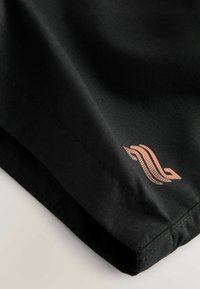 Angolo di un capo di tessuto nero caratterizzato da una superficie liscia e un logo in tonalità rame con linee curve e punti. La cucitura è ordinata e ben rifinita.