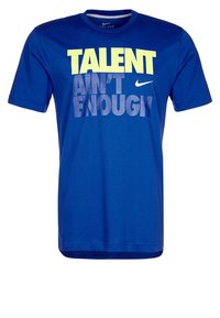Blå kortärmad t-shirt i mjukt tyg. Har fet tryckt text i gult och grått: "TALANG ÄR INTE TILLRÄCKLIG." Nike-logga närvarande.