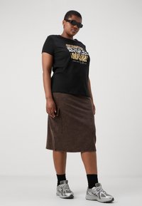 Tricou scurt cu mânecă negru, cu grafică de imprimeu animal aurie, asociat cu o fustă de lungime până la genunchi, de culoare maro, care are un buzunar lateral și o finisare texturată.