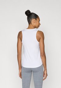 Λευκό αμάνικο τοπ από ομαλό ύφασμα, με στρογγυλή λαιμόκοψη και ελαφρώς καμπυλωτό τελείωμα. Φορεμένο με ανοιχτό γκρι κολάν.