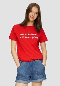Rode katoenen T-shirt met de witte tekst "un croissant s'il vous plaît," gecombineerd met denim shorts. Het T-shirt heeft korte mouwen en een ronde hals.