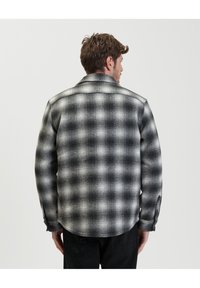 Camicia di flanella a quadri bianco e nero con collo e polsini con bottoni. Presenta un motivo testurizzato e un orlo dritto sul retro.