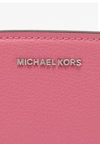 Ροζ υφή δέρματος με ασημί λογότυπο "MICHAEL KORS" που είναι ανάγλυφο στην επιφάνεια. Οι ραφές προσθέτουν λεπτομέρεια και ενισχύουν την εκλεπτυσμένη εμφάνιση του υλικού.