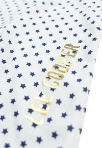 Tissu blanc présentant un motif de petites étoiles bleu marine, avec l'inscription "LEE COOPER" en lettres métalliques dorées. La texture semble lisse et douce.
