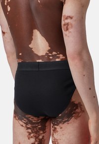 Svarta simbyxor med en enkel design. Har en texturerad midjeband och en slät yta. Huden visar variationer i ton och mönster.