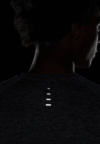 Camiseta atlética oscura con escote redondo y una fila de recortes reflectantes en la parte superior de la espalda, que resalta la textura de la tela.