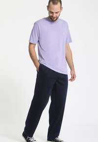 T-shirt en coton violet avec un col rond, associé à un pantalon en velours côtelé bleu marine. Des baskets noires complètent la tenue, offrant une coupe décontractée.