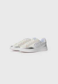 Sneakers bianchi con tomaia in pelle, accenti argentati sulla punta e sul tallone, lacci piatti e dettagli perforati sui lati.