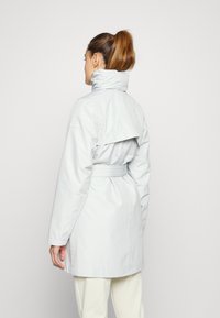 Abrigo impermeable de color gris claro con cuello alto, cintura ceñida y detalle de capa trasera. Presenta mangas largas y una tela lisa y texturizada.