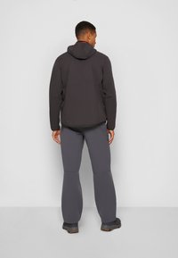 Zwarte capuchonjack met een soepele textuur, gecombineerd met grijze broek met een ruime pasvorm en duurzaam materiaal. Zichtbare stiksels op de jas.