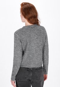 Pulover gri, pufoș, tricotat, cu guler rotund și mâneci lungi, asociat cu blugi închiși la culoare, cu talie înaltă. Design simplu, fără modele.