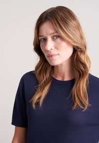 Granatowy sweter z krótkim rękawem i okrągłym dekoltem, wykonany z miękkiego materiału, charakteryzujący się luźnym krojem i gładką teksturą.