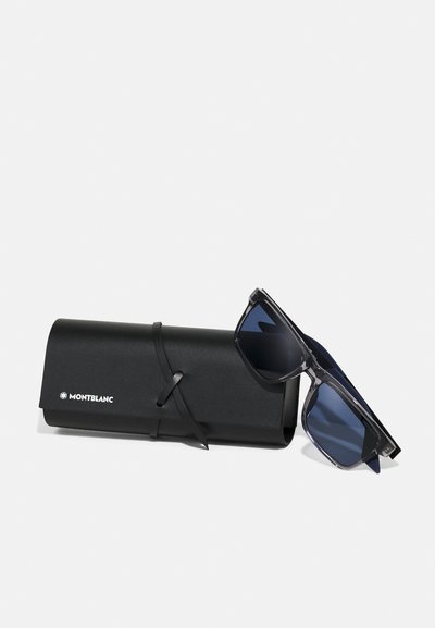 Sorte Montblanc solbriller med blå linser, hvilede mod et sort læder Montblanc-etui bundet med en læderrem på hvid baggrund.