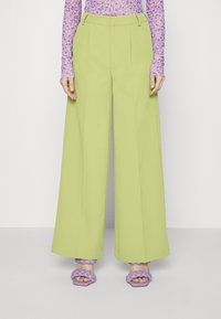 Limetkově zelené kalhoty s širokými nohavicemi a předními sklady, spárované s levandulovými pletenými sandály. Fialový top s dlouhým rukávem a květinovým vzorem.