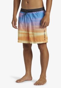 Shorts de bain pour hommes dans des dégradés de bleu, orange et jaune, avec une taille élastique à cordon de serrage et un logo sur le côté.