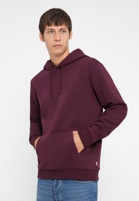 Bordeaux hoodie met een voorzak, trekkoordkap en ribgebreide manchetten. Zachte stoftextuur, losse pasvorm, gecombineerd met lichtblauwe spijkerbroeken.