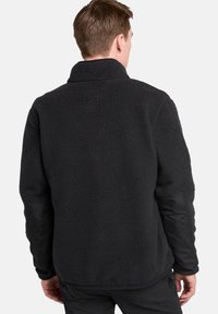 Giacca in fleece nera con un'esterno textured, collo alto e maniche lisce a contrasto. Presenta una vestibilità comoda e nessun marchio visibile.