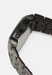 Orologio in metallo nero con cassa rettangolare, pulsanti testurizzati e bracciale a maglie. Presenta una finitura liscia e una corona prominente.