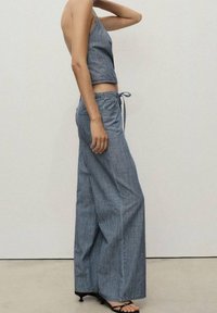 Haut court en jean rayé et pantalon à jambes larges, avec une taille nouée, un tissu texturé et une coupe décontractée. Le schéma de couleurs comprend des rayures bleues et blanches.