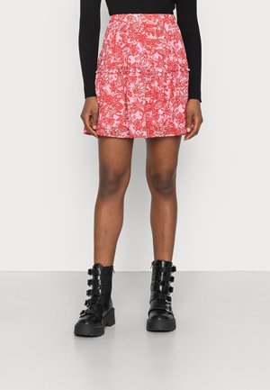 Jupe à motif paisley rouge et rose avec une taille froncée, stylée avec des bottines en cuir noir à chevilles dotées de plusieurs sangles et boucles.