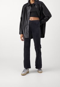 Black satin oversized shirt, fitted black top, navy flared pants, gray sneakers with a light sole, and textured fabric details throughout.