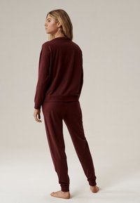 Bordowy zestaw odzieży domowej składający się z luźnej długo rękawowej bluzki i zwężanych spodni, oba wykonane z miękkiego, texturaowanego materiału.