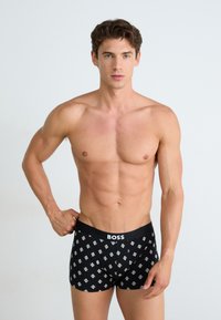 Boxer shorts noirs avec un motif géométrique répétitif en blanc, dotés d'une ceinture douce affichant le nom de la marque "BOSS" en lettres blanches.