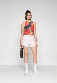 Spordikas punase ja musta ombre-kavandiga lühike top, mida on kombineeritud valgete lühikeste pükstega. Modell hoiab musta veepudelit ning kannab valgeid sokke ja spordijalatseid.