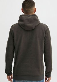 Sudadera de felpa gris con una gran capucha, textura suave y puños acanalados. Presenta un corte holgado y un dobladillo recto.