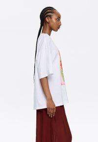 Camiseta blanca de gran tamaño con un diseño gráfico colorido. Mangas cortas, escote redondo, combinada con una falda fluida burdeos. Textura suave.