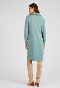 Abito lavorato a maglia di un blu chiaro con colletto a coste, maniche lunghe e silhouette al ginocchio. Indossato con stivali al ginocchio beige.
