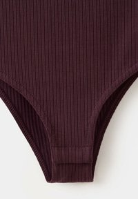 Gros plan d’un bas de maillot de bain en tissu côtelé violet foncé avec bords cousus et détail de couture sur fond blanc.