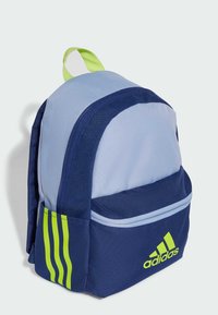Mochila de color azul marino y celeste con un acento verde. Presenta tres franjas verdes y un logo de Adidas. Hecha de tela duradera con un pequeño asa.
