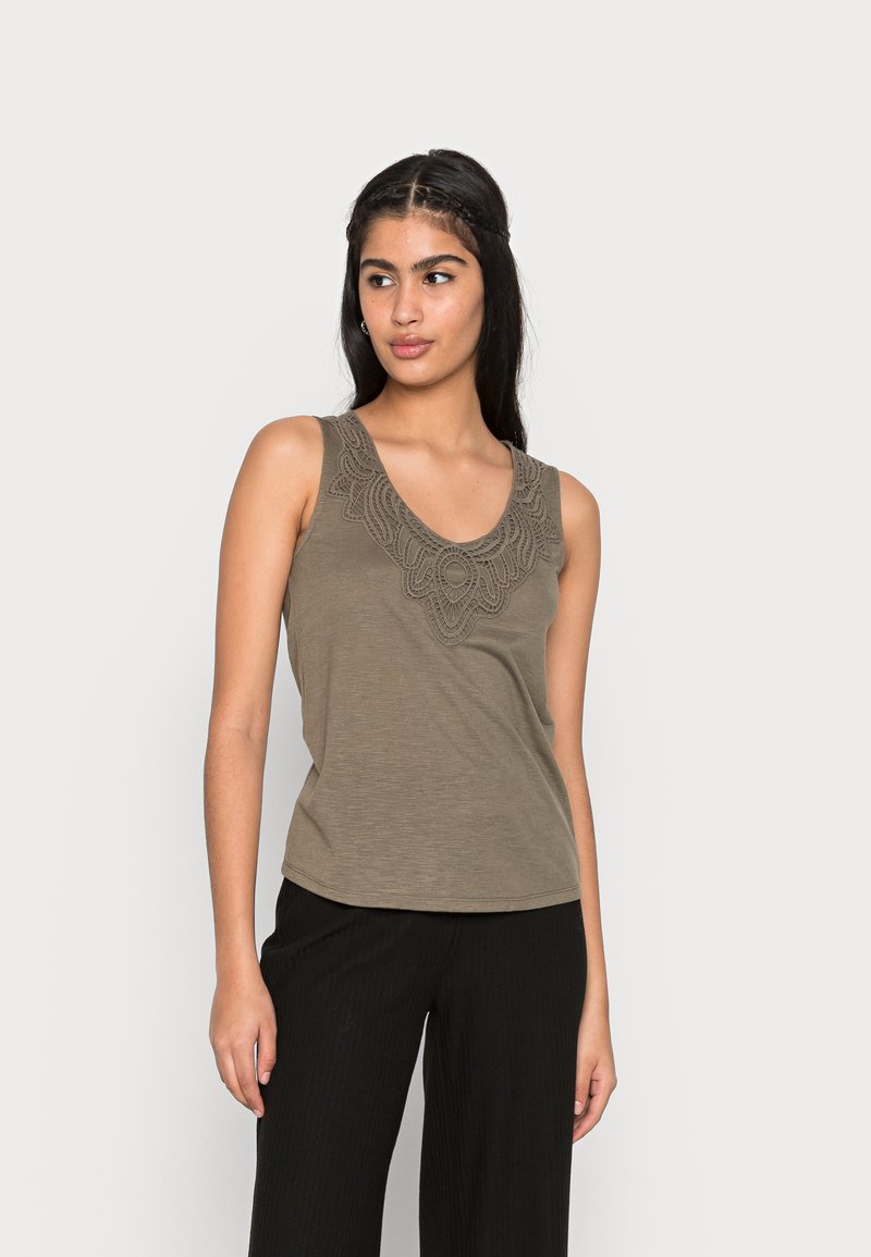 Top sem mangas bege com um decote profundo em forma de scoop e detalhes intrincados em renda texturizada ao redor do colarinho. Tecido suave, ajuste descontraído.