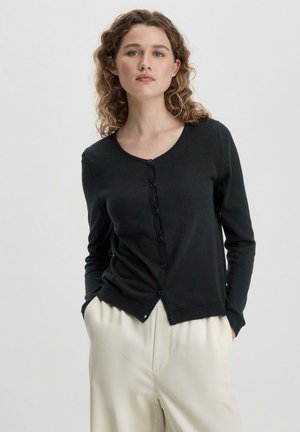 Zwarte cardigan met een ronde hals, een knoopsluiting aan de voorkant, lange mouwen en geribbelde manchetten, gecombineerd met lichtgekleurde broeken.