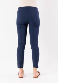 Pantaloni aderenti blu navy con una superficie liscia, vita media e lunghezza alla caviglia, abbinati a sandali flat marroni.