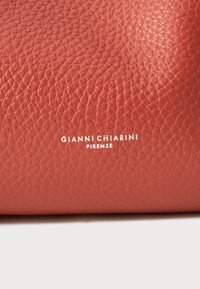 Sarkans teksturēts ādas soma ar izteiksmīgu izsistā logotipu "GIANNI CHIARINI FIRENZE" baltā krāsā, ar gludu apdari un bagātu krāsu.