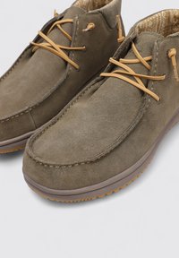 Zapatos de ante marrón con suelas de goma, con cordones de cuero beige y un forro interior con estampado. Punta redonda con detalles cosidos.