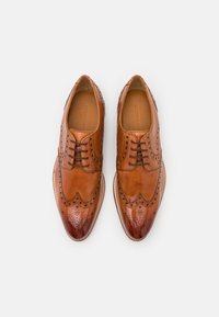 Hnědé kožené brogue boty s podrobnými perforacemi, designem wingtip a lesklou špičkou. Šněrovací styl s hladkým povrchem.