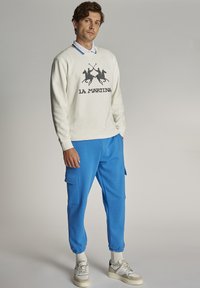 Bela mikica s grafiko dveh polo igralcev, v kombinaciji s svetlo modrimi hlačami za tek, ki imajo stranske žepke in elastične manšete.