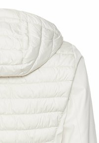 Witte pufferjack met een gewatteerd patroon, voorzien van een capuchon en een gladde textuur, benadrukt door een gestroomlijnd, modern ontwerp.