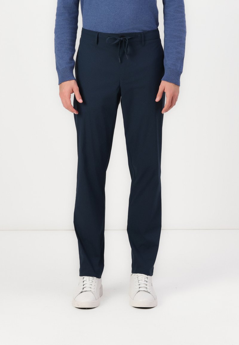 Námořnické modré lehké kalhoty s šňůrkou v pase, slim fit a hladkou texturou. Kombinované s bílými teniskami.