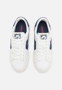 Paire de baskets Levi's blanc et marine avec des lacets blancs, intérieur marine et logo Levi's rouge sur les semelles intérieures et les étiquettes de la languette.