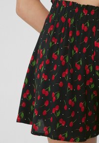 Černá sukně s elastickým pasem, zdobená vzorem červených třešní a zelených listů, kterou nosí osoba.