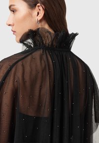 Czarna przezroczysta tkanina z marszczonym kołnierzem ozdobiona małymi srebrnymi koralikami, z marszczeniami przy dekolcie i luźno opadającymi fałdami.