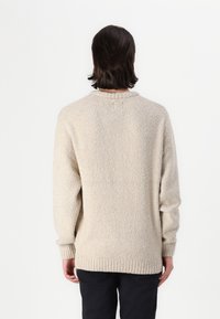 Beige knit sweater with a textured, fuzzy fabric, ribbed cuffs, and hem. Crew neckline, relaxed fit, and back view shown.