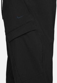 Czarne spodnie cargo z podwójnymi przednimi kieszeniami, teksturowana tkanina i małe niebieskie logo Nike. Prosty krój z wzmocnionymi przeszyciami.